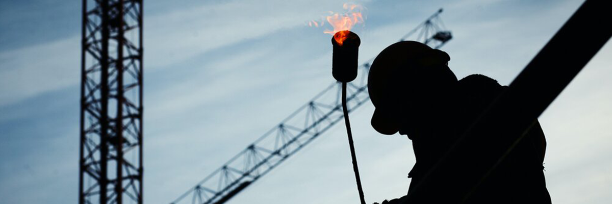 A photograph of a person in silhouette. They are wearing a hard hat and are on a construction site.