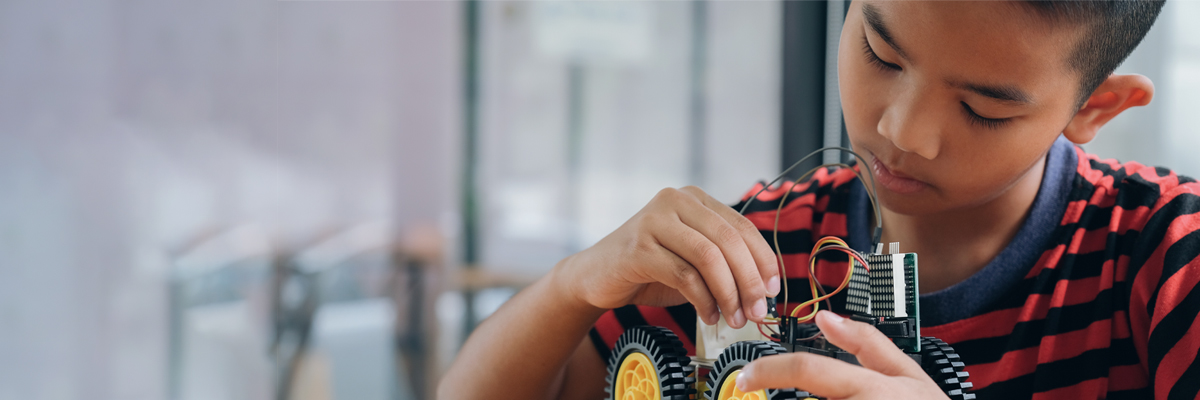 A photograph of a young, asian boy working on some wiring in an engineering assignment.