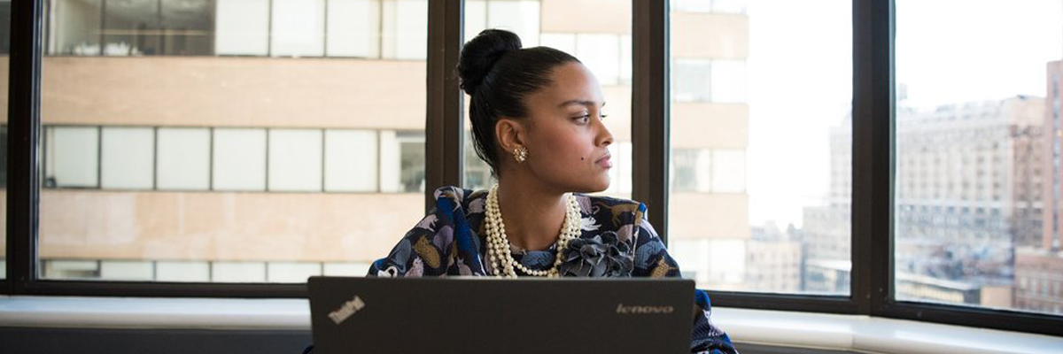 An image of a woman of colour using a computer while thinking about her work.