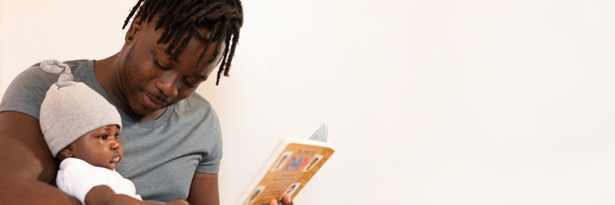 A photograph of a man reading a book to his infant child.