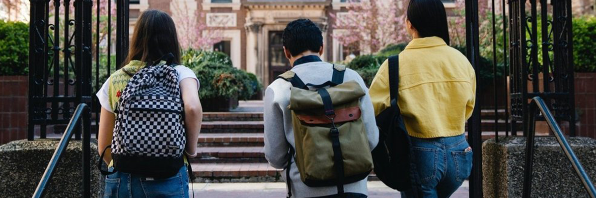 A photograph of three post-secondary students from behind walking into their school.