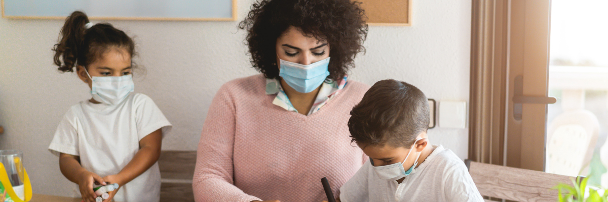 Photographic image of a teacher helping children and all people are wearing masks